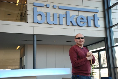 Blinder junger Mann mit dunkler Brille und Langstock vor einem Firmengebäude